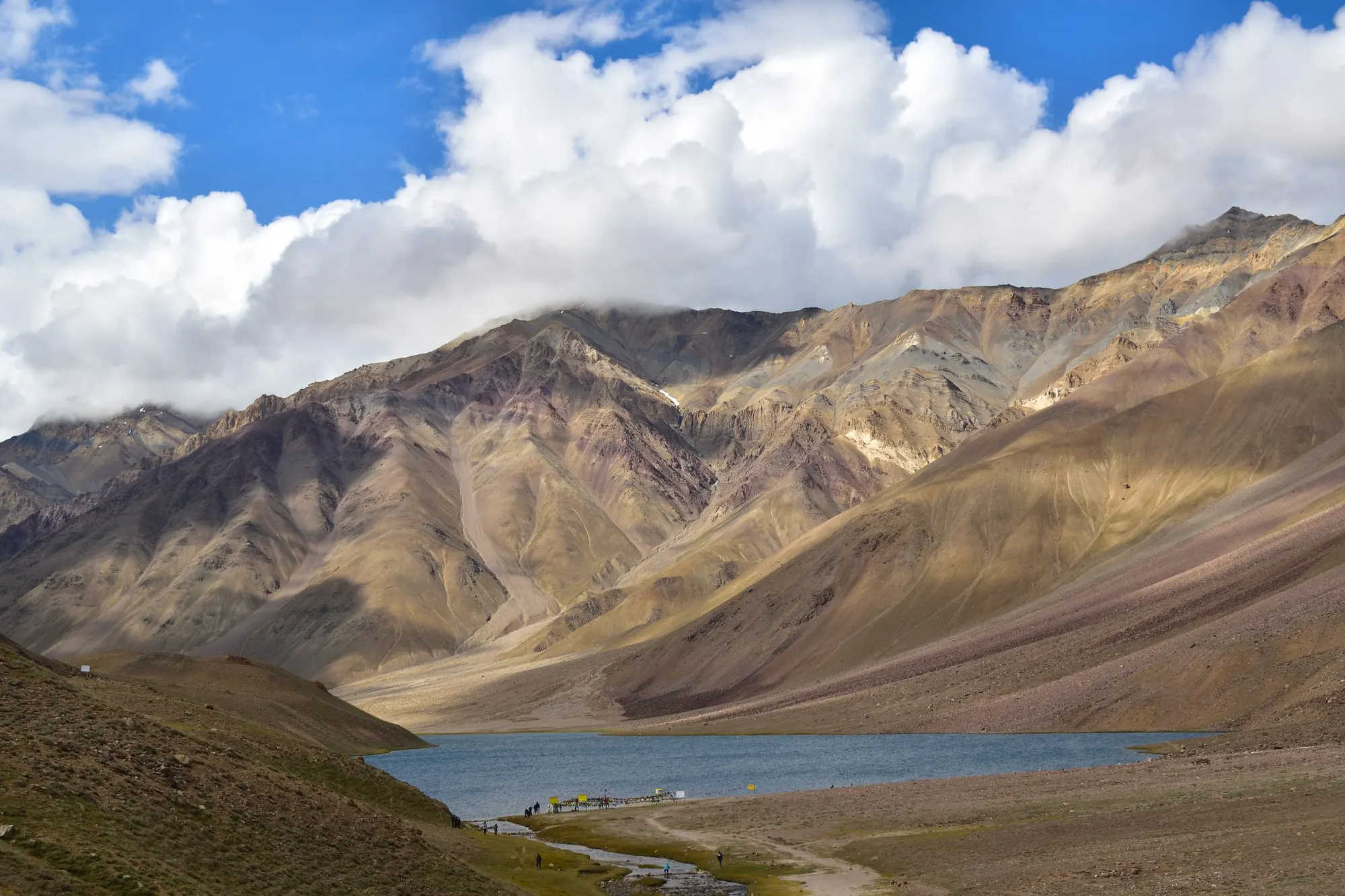 Chandratal lake between brown mountains under a cloudy sky